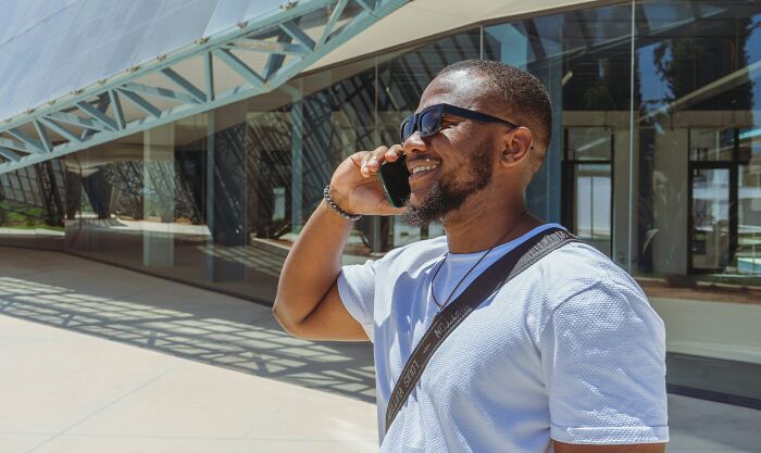 Man smiling and talking on phone outdoors near modern building, experiencing shocking moments people have lived through.