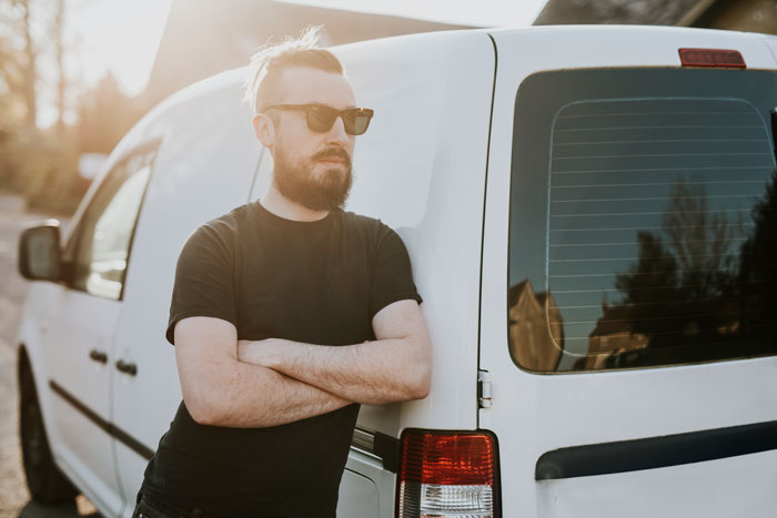 Man with beard and sunglasses leaning against a white van, reflecting on a dog almost stolen by kids at the park incident.