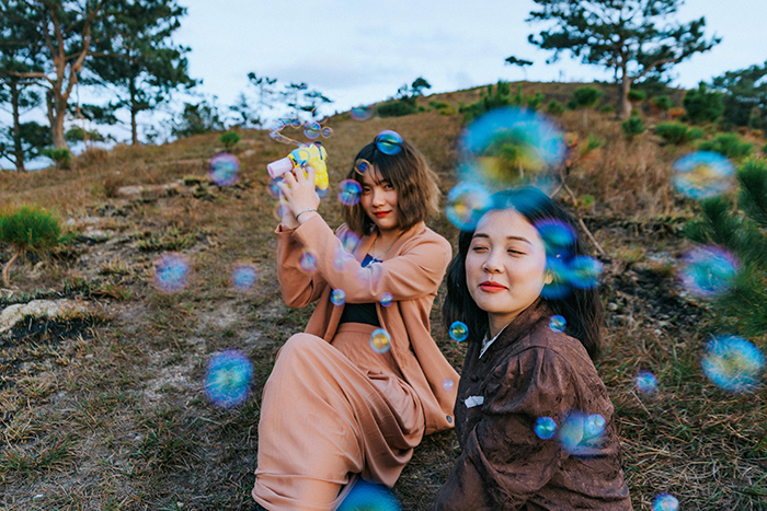 Two women sitting outdoors surrounded by bubbles, illustrating the maid of honor missing sister&rsquo;s wedding after losing dog.