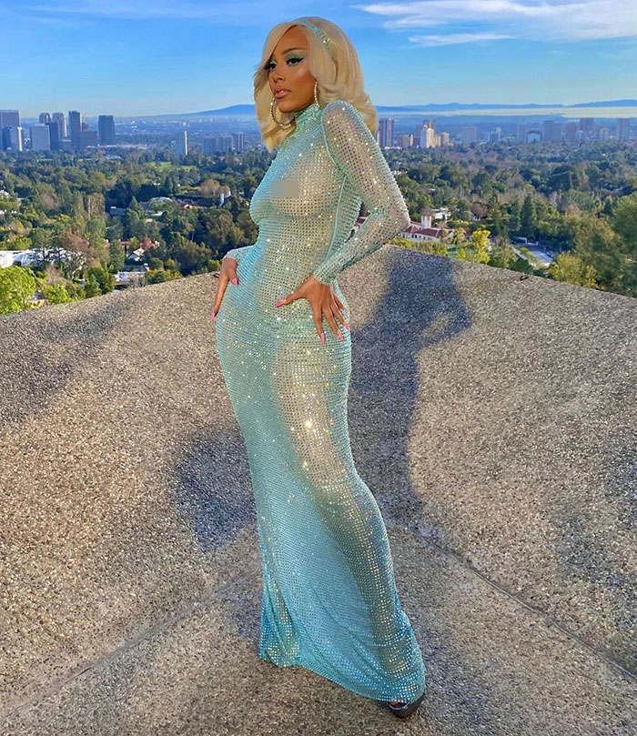 Doja Cat in a sparkling blue gown posing outdoors with cityscape background, highlighting plastic surgery mishap. Doja Cat in a sparkling blue gown posing outdoors with cityscape background, highlighting plastic surgery mishap.
