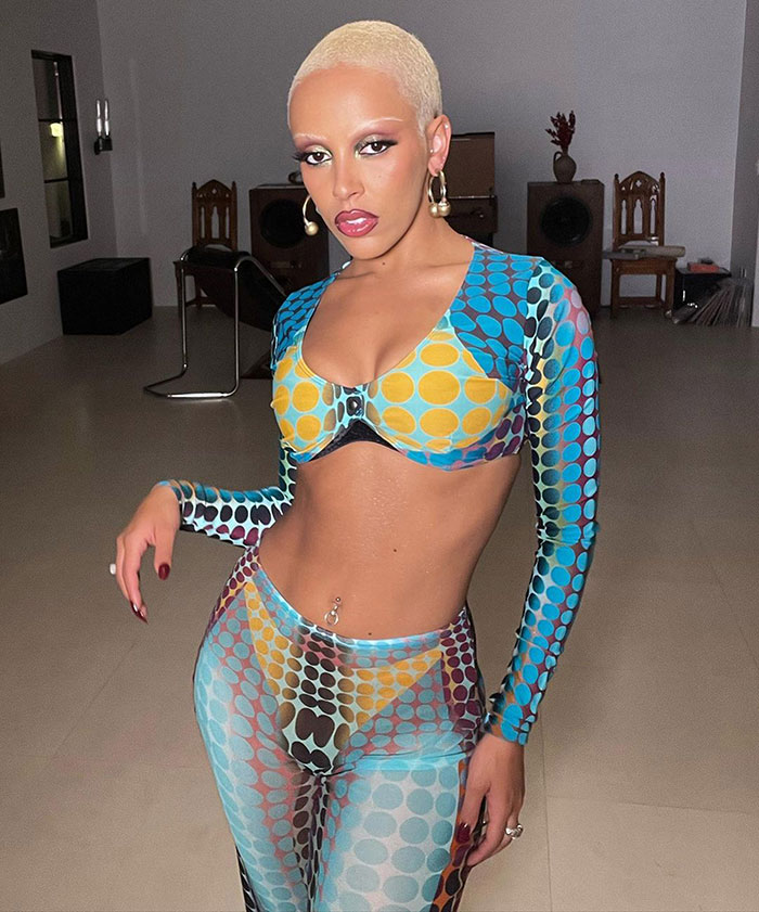 Doja Cat posing indoors wearing a colorful patterned outfit, highlighting a plastic surgery mishap on the red carpet. Doja Cat posing indoors wearing a colorful patterned outfit, highlighting a plastic surgery mishap on the red carpet.