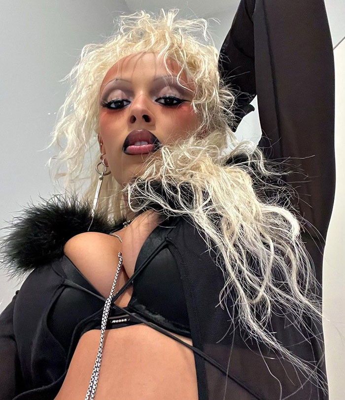 Doja Cat with blonde hair and bold makeup posing in a black outfit, related to plastic surgery mishap on red carpet. Doja Cat with blonde hair and bold makeup posing in a black outfit, related to plastic surgery mishap on red carpet.