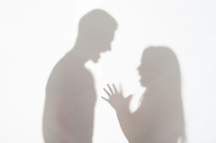 Silhouettes of a man and woman arguing passionately, illustrating domestic violence debate between genders.