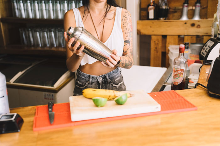 Female student shaking cocktail shaker in kitchen, preparing drinks amid roommate sleep aid suspicion.