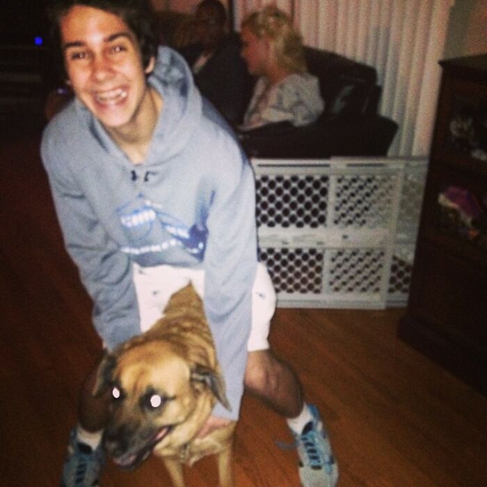 Young man in a hoodie happily playing with a dog indoors, capturing a nostalgic celebrity Instagram moment.