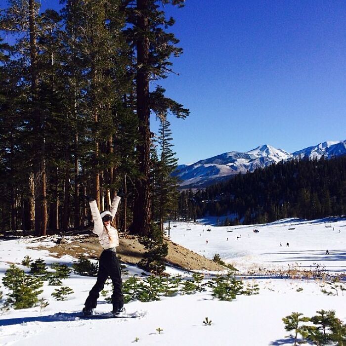 Person snowboarding in a snowy mountain landscape with tall trees and clear blue sky, Instagram posts celebrities style.