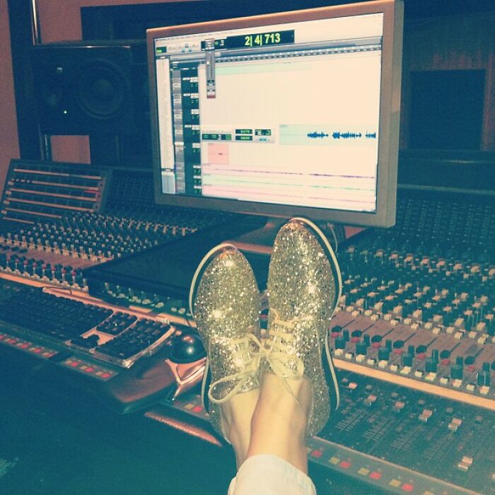 Person wearing glittery shoes with feet up on audio mixing console in a music studio recording session, showcasing celebrity posts.