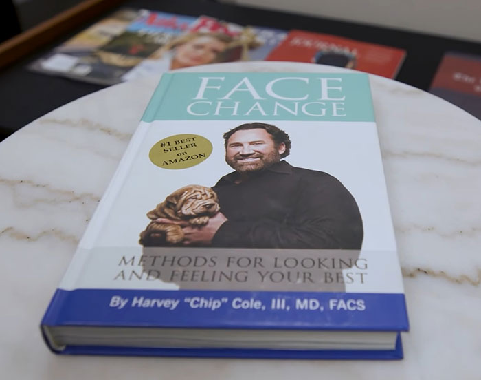 Book titled Face Change by a plastic surgeon displayed on a marble table, highlighting facial enhancement methods.