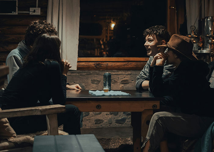 Group of friends sitting around a table at night, with a man admitting he found his wife repulsive on their first date.