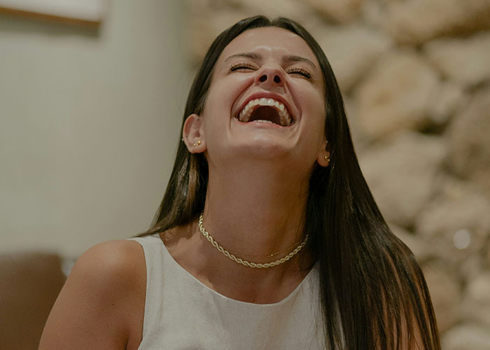 Woman with long dark hair laughing joyfully indoors, illustrating emotions linked to man admits he found wife repulsive on first date.