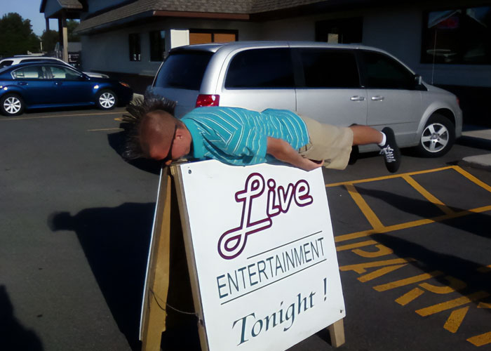 Person with a mohawk doing a plank on a live entertainment sign, showcasing a dumb fad participated in for fun.