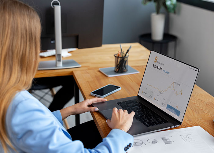 Person analyzing Bitcoin price trends on a laptop displaying financial charts and market data at a wooden desk.