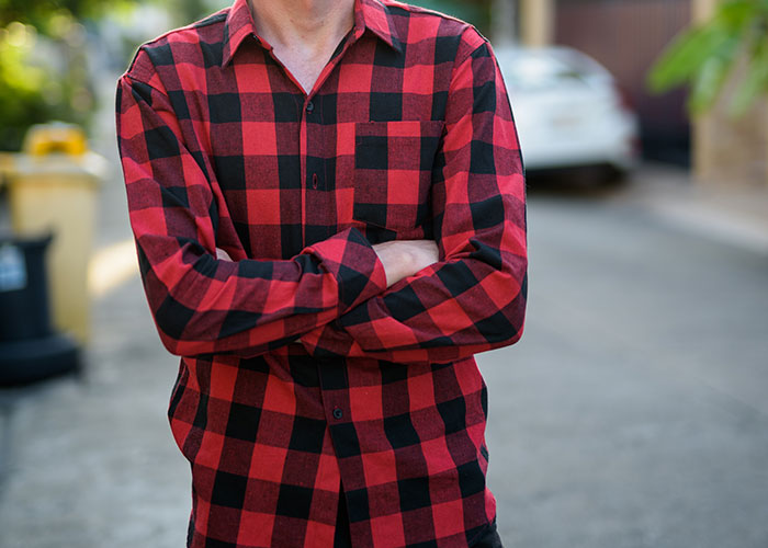 Person wearing red and black checkered shirt with arms crossed standing outdoors discussing dumbest fad participated in.