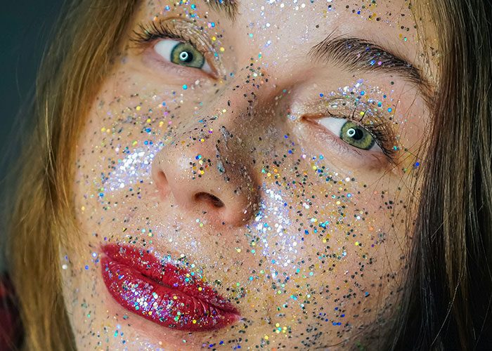 Close-up of a woman with glitter on her face and bright red lipstick, illustrating a popular dumbest fad participation.