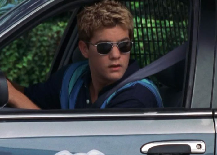Teenager wearing sunglasses sitting in a car, reflecting on the dumbest fad they participated in.