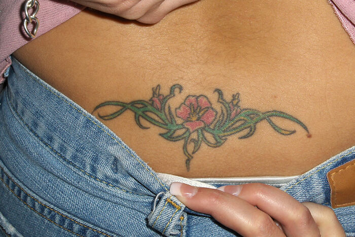 Lower back floral tattoo on a person wearing blue jeans, representing a popular dumbest fad many participated in.