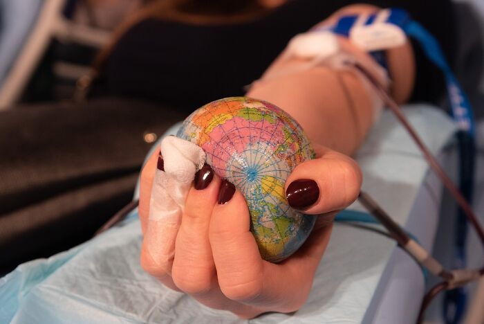 Person donating blood holding a small globe stress ball, illustrating mind-boggling beliefs smart people still support.