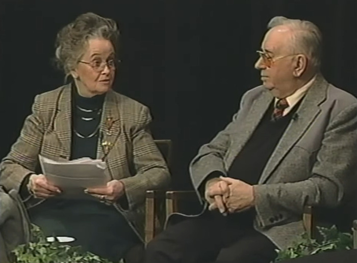 Two elderly people discussing the haunted Annabelle doll's chilling history in a small indoor interview setting.