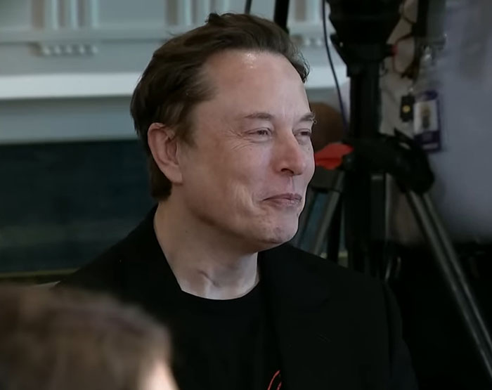 Elon Musk in a black jacket smiling during an indoor event, related to Tesla CEO search updates and leadership changes.