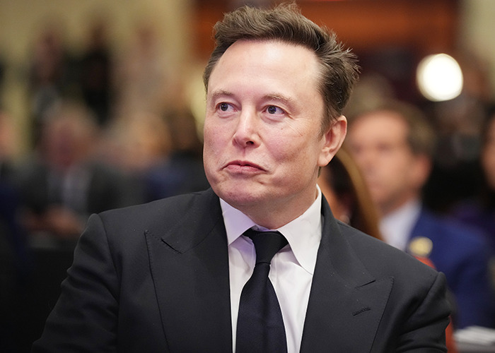 Elon Musk in a black suit and tie at a formal event, related to his trans daughter Vivian's modeling debut buzz.