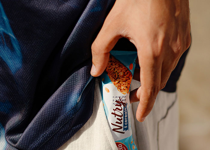Hand putting a Nutty 5 cereals snack bar into a pocket, illustrating parents sharing the worst things kids did in public.