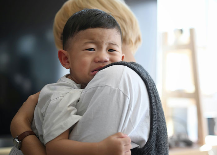 Upset child clinging to parent in public, capturing the worst things kids did that made parents want to disappear.
