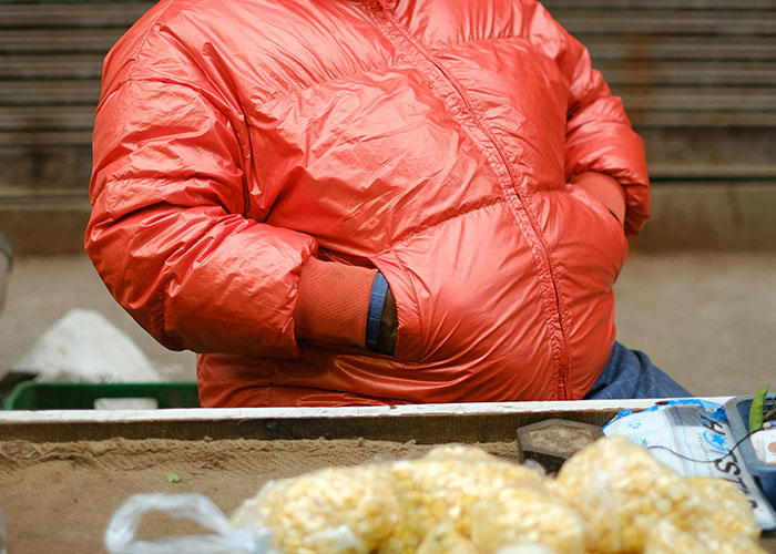 Parent wearing a red jacket with hands in pockets, sitting near a table with food, illustrating kids embarrassing parents in public.