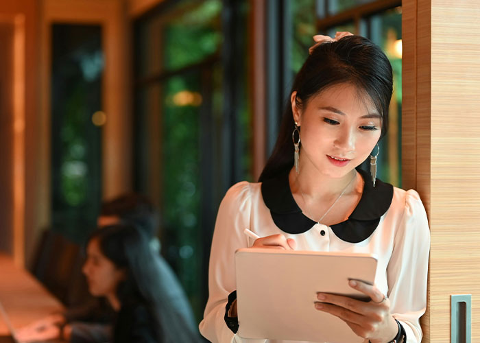 Young woman writing on a tablet in a cozy café, representing parents sharing the worst things their kids did in public.