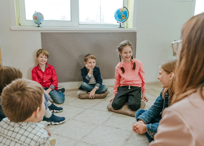 Group of children sitting on the floor with an adult, illustrating parents sharing the worst things their kids did in public.
