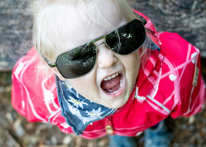 Child wearing sunglasses and red jacket shouting outdoors, illustrating worst things kids did in public moments for parents.