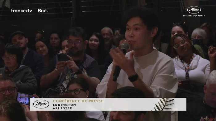 Reporter holding a microphone asking a question during Cannes Festival where Emma Stone responds to her real name usage.