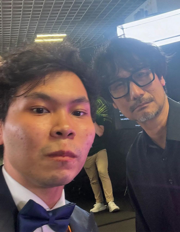 Two men posing for a close-up selfie, with focus on Emma Stone responding to reporter at Cannes event.