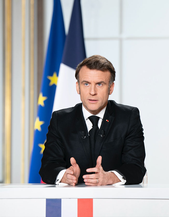Emmanuel Macron speaking at a formal event with French and European Union flags in the background, grooming rumors context. Emmanuel Macron speaking at a formal event with French and European Union flags in the background, grooming rumors context.