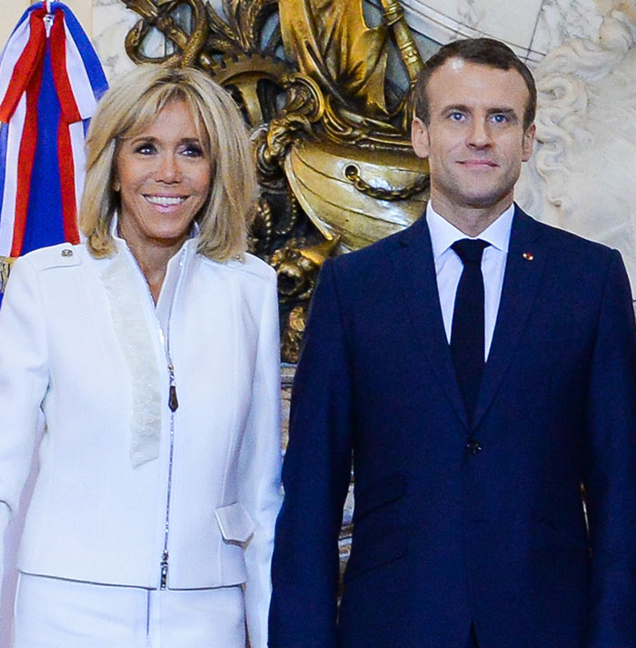 French President Emmanuel Macron and his wife standing together at a formal event with decorative background elements.
