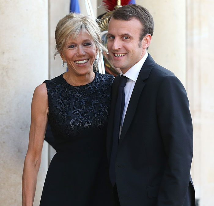 French President Emmanuel Macron with his wife smiling, related to lip reader revealing words after shoving incident.