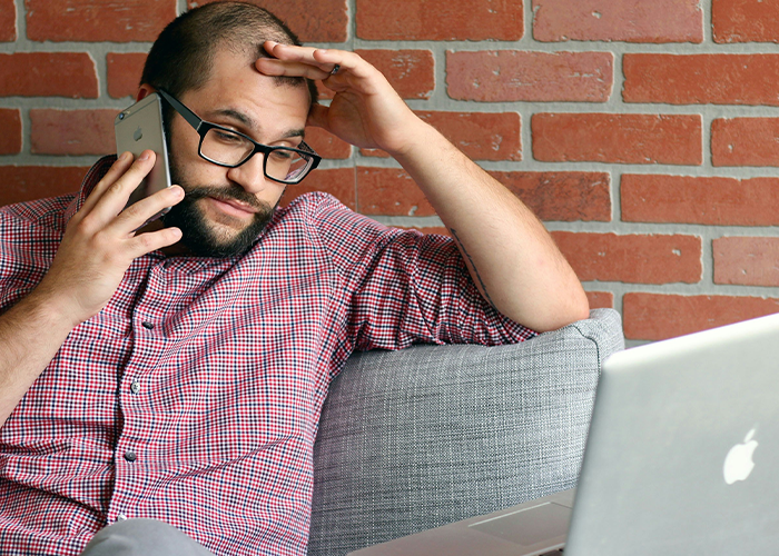 Engineer in glasses looks frustrated on a call while sitting on a couch with laptop, reflecting on difficult treatment.