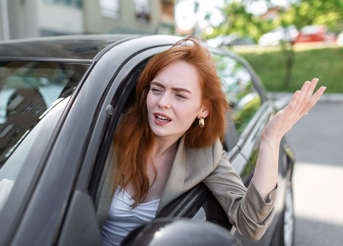 Woman angrily gesturing from car window while trying to save a parking spot for hubby and getting kicked out.