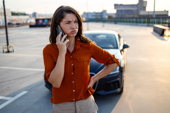 Woman in orange shirt standing in parking spot on phone, frustrated while saving parking spot for hubby in lot.