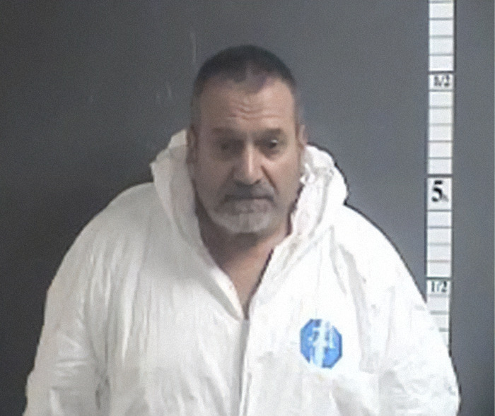 Mugshot of a man wearing a white forensic suit standing against a height measurement background.