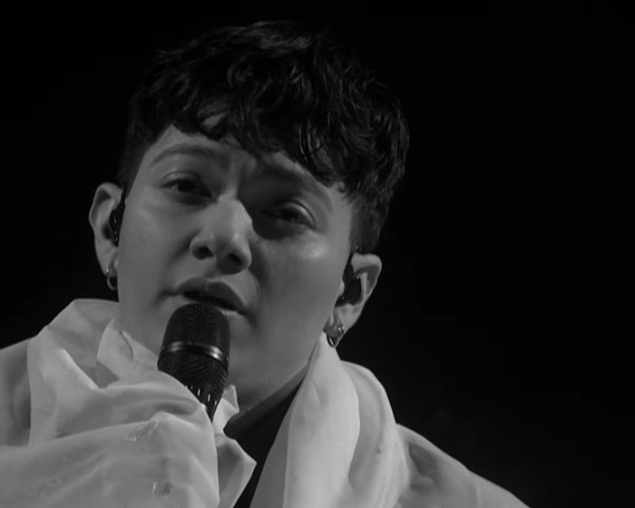 Close-up of Austria's Eurovision 2025 performance with the singer holding a microphone against a dark background.