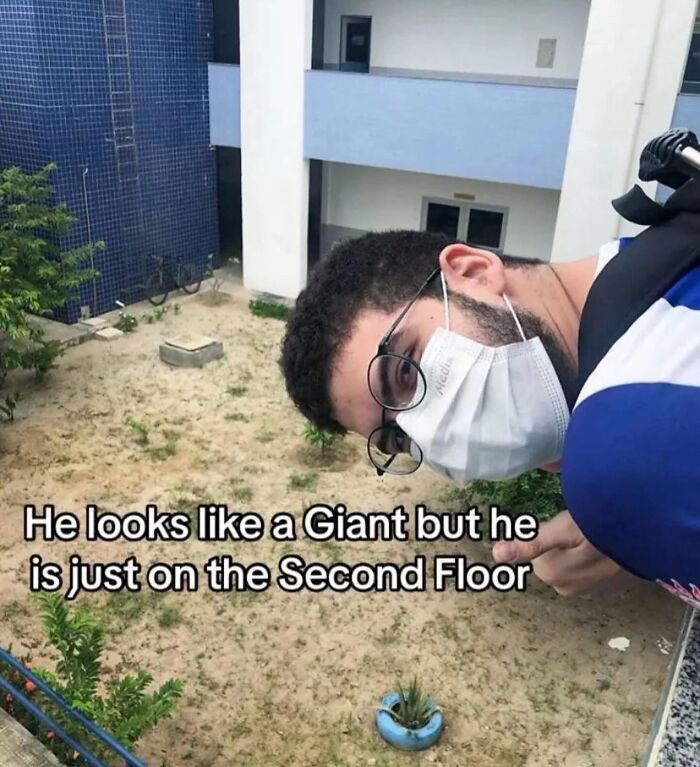 Man wearing glasses and a mask leaning over a balcony, creating an optical illusion of giant size inside Big Ben.