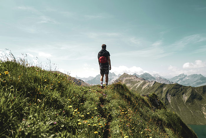 Person with a red backpack hiking on a grassy mountain trail, reflecting on memories of an ex-fiance Valentine Day.