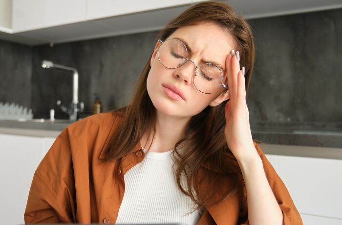 Young woman with glasses looking stressed, representing jealous grandparents upset about ex-in-laws giving money to kid.