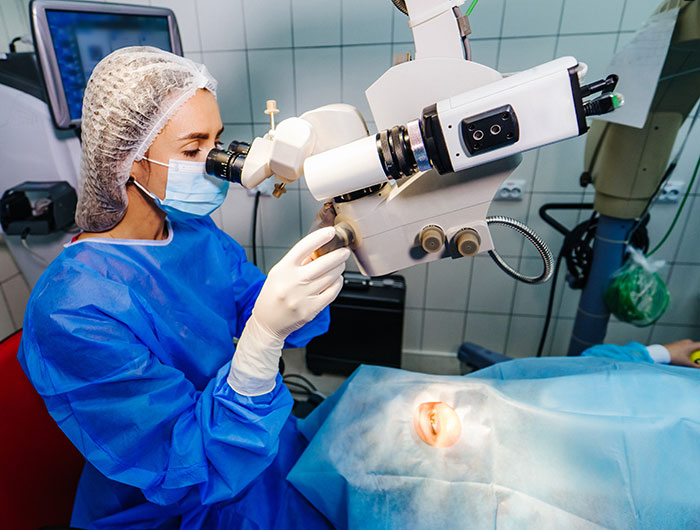 Surgeon in protective gear performing LASIK eye surgery using advanced microscope and laser equipment in clinic room.