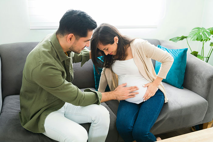 Couple at home, man touching pregnant woman’s belly, illustrating pregnancy and birth facts and experiences.