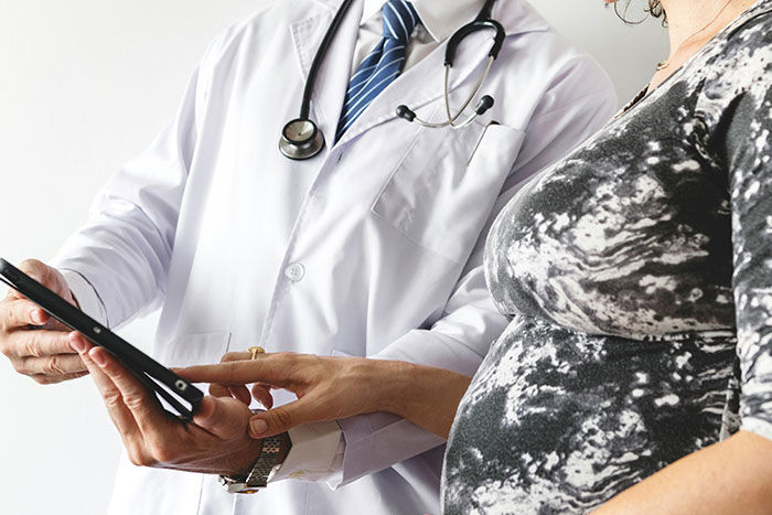 Doctor with stethoscope showing digital tablet to pregnant woman during prenatal consultation about pregnancy and birth facts.