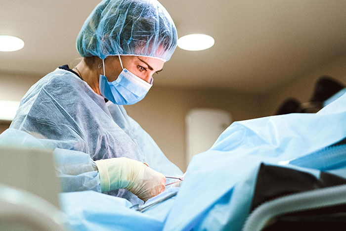 Medical professional wearing protective gear performing a procedure related to pregnancy and birth in a clinical setting.