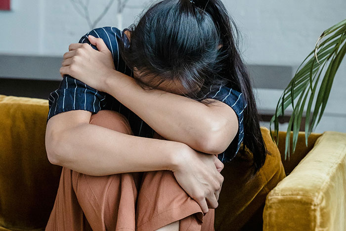 Woman sitting on couch with head down and arms wrapped around knees depicting emotional struggle of pregnancy and birth facts