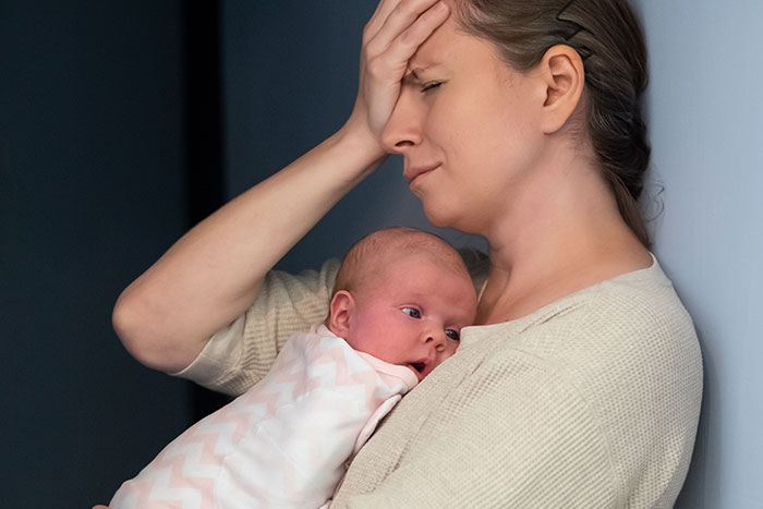 Stressed woman holding newborn baby, showing emotional and physical challenges of pregnancy and birth facts.