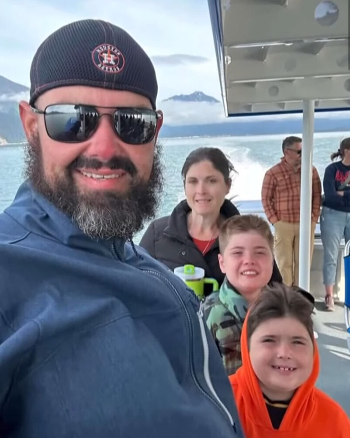 Family of four smiling on a boat with mountains and water in the background before boating tragedy occurred.